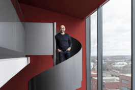 Portrait des Geschäftsführers des Dortmunder U Edwin Jacobs. Stehend auf der Wendeltreppe des Archivs mit Blick durch die Fensterfront auf Dortmunder Skyline.