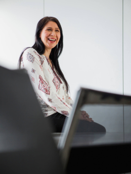 Mitarbeiterportrait für einen Geschäftsbericht. Mitarbeiterin sitzt lachend auf dem Tisch eines Konferenzraums und lacht in Richtung eines Gesprächspartners.