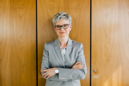 Businessportrait einer leitenden Angestellten. Lehnt mit verschränkten Armen an eine Holzwand.