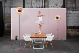 Produktfotografie. Ballerina steht auf Fussspitzen auf einem Tisch und schaut zu einem Nussknacker. Im Hintergrund steht eine deplaziert wirkende rosa Wand.