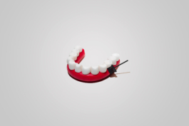 Stilllifefotografie eines comicartigen Gebiss an dem ein fliegender Besen die Zwischenräume reinigt.