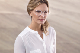 Werbefotografie einer Dame mit edler Brille mit weissem Rahmen vor undefiniertem, warmen Hintergrund.