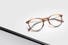 Stilllifeaufnahme einer edlen Brille der Marke Morel. Die Brille liegt auf einem weissen Podest auf grauem Hintrund.