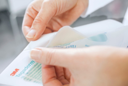 Imagefotografie eines Medizinischen Hilfsmittels. Zwei feminine Hände öffnen die Verpackung eines sterilen Wundpflasters