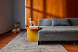 Produktfotografie eines gelben Beistelltisches in moderner Retro Location. Auf dem Beistelltisch der Marke Feli steht stylische Deko. Sonneneinfall durch ein Fenster erzeugt eine stimmungsvolle Dramatik.
